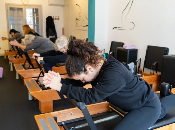 Instructor corrigiendo la postura de una alumna en Pilates Reformer